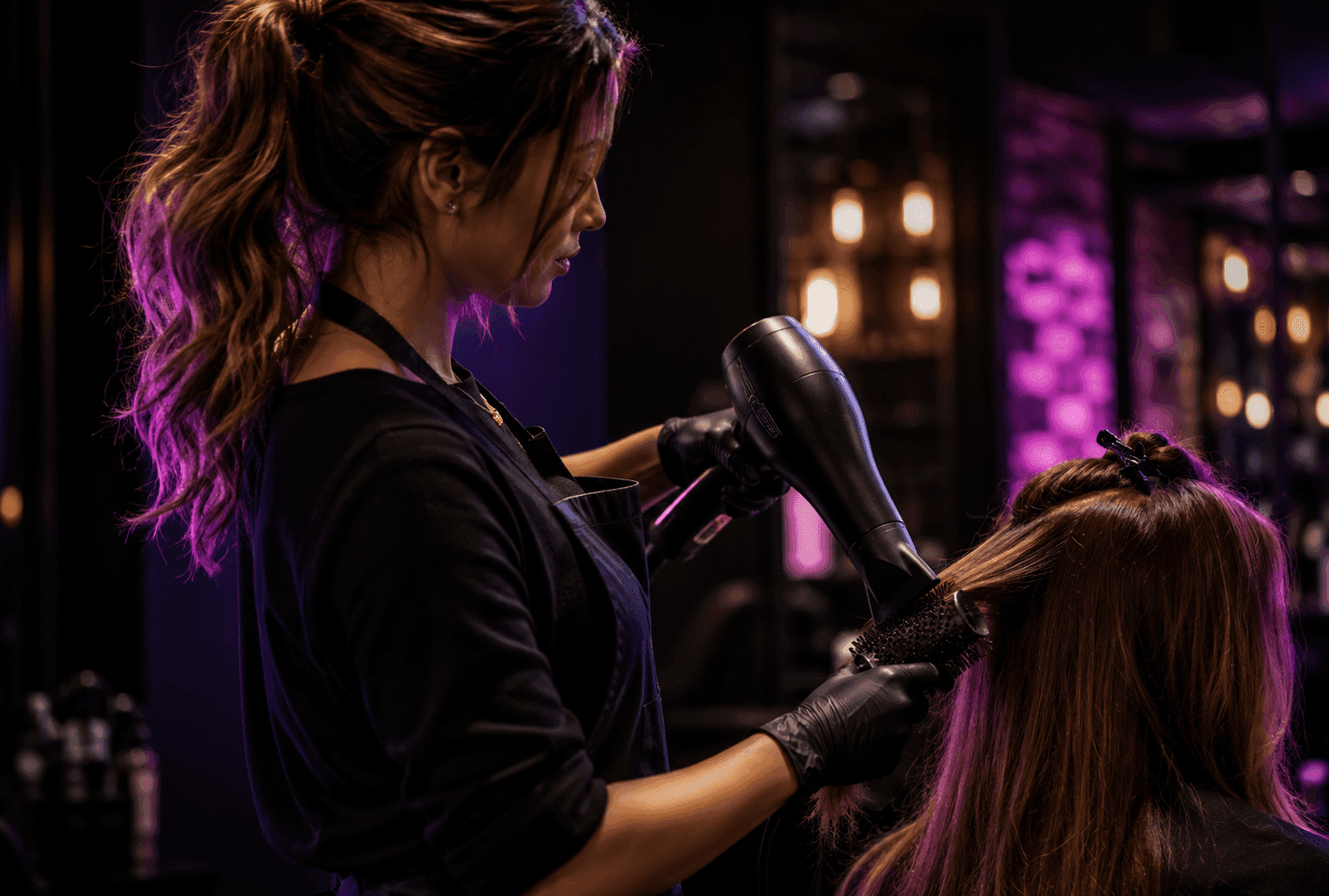 Hairstylist mid-blowout at the chair with a round brush and dryer